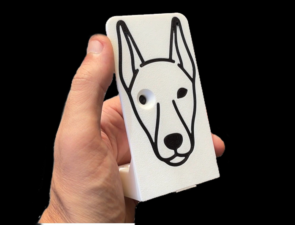 The printed Bark Cam shell held in one hand — white body with the dog face inlaid in black